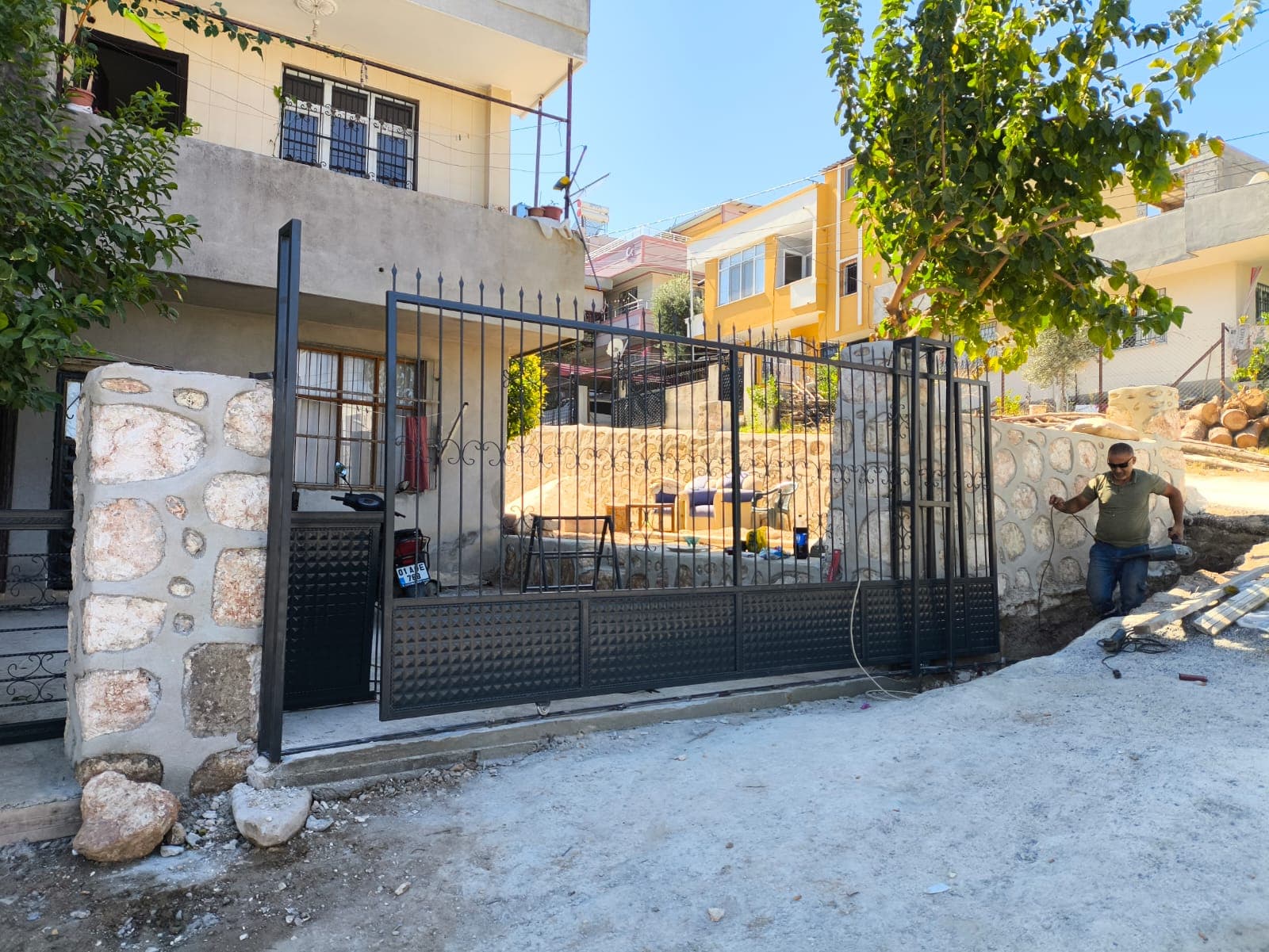 Taş bahçe duvarları arasında siyah metal giriş kapısı