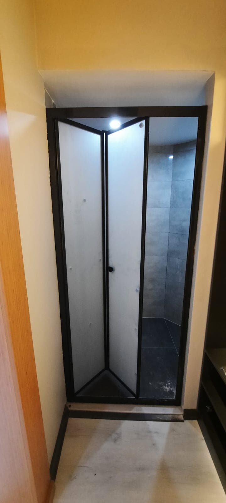 Dar duş alanında koyu çerçeveli katlanır kapı
