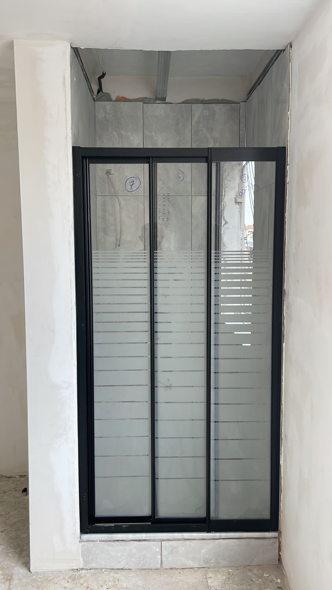 Dar niş içine yerleştirilmiş koyu çerçeveli duş kapısı