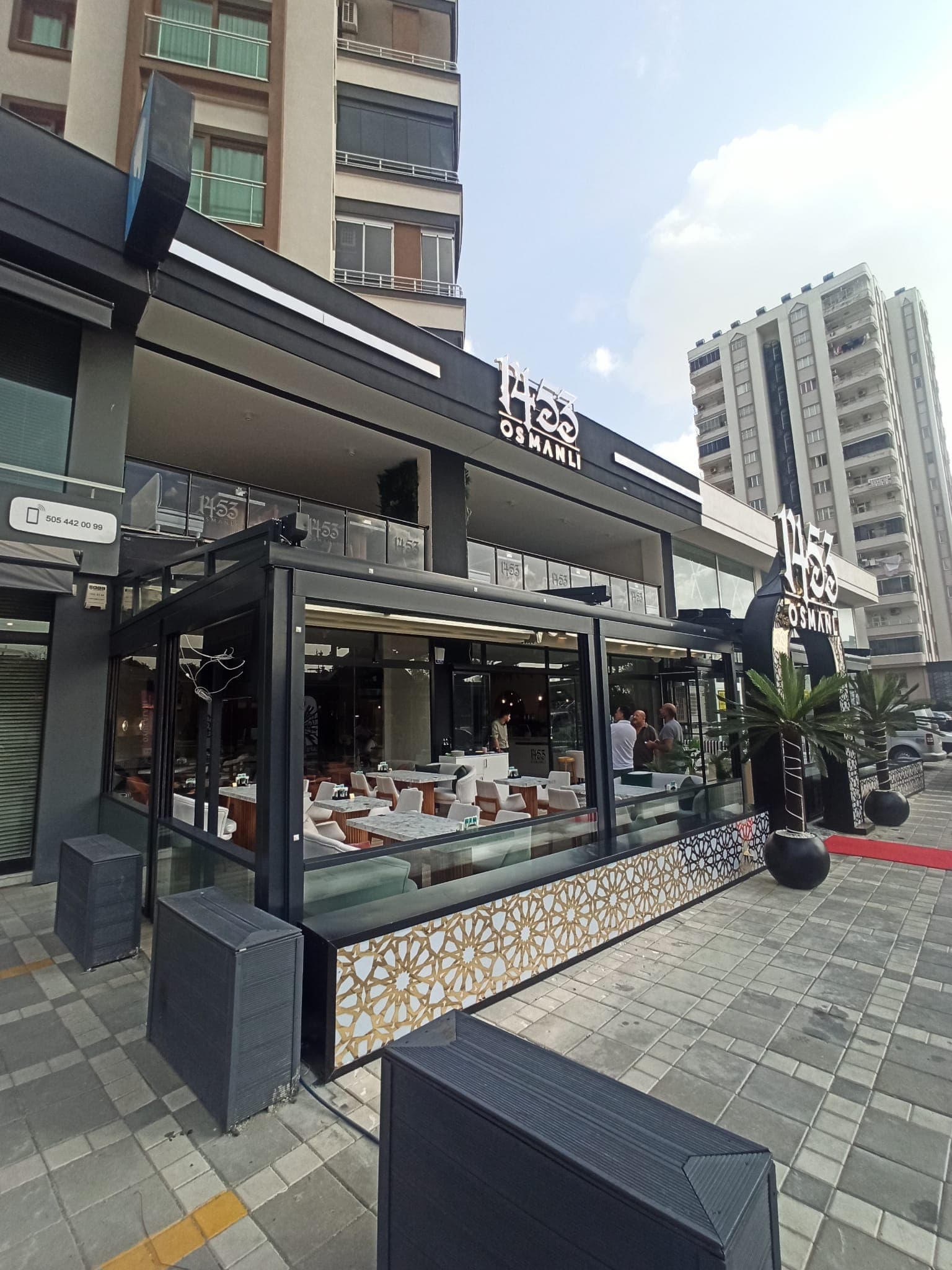Kafe önündeki koyu çerçeveli cam kapamanın yandan görünümü