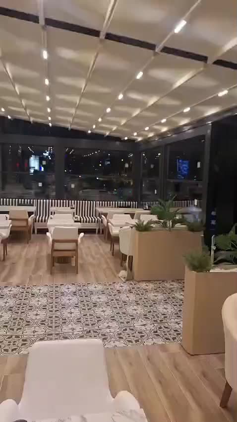 Aydınlatmalı tavan altında masa ve sandalyelerin bulunduğu kapalı oturma alanı