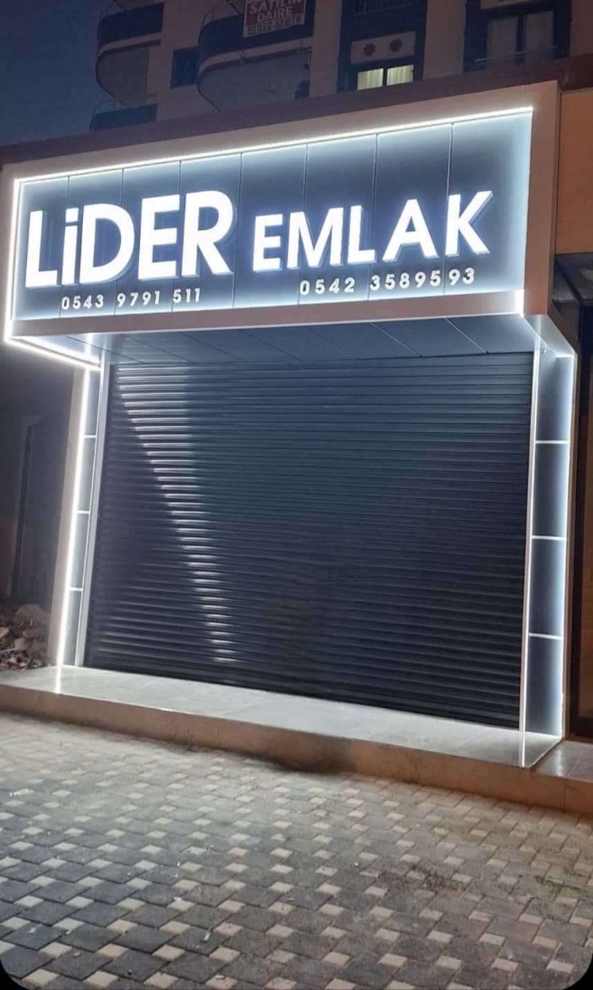 Aydınlatmalı tabela altında koyu kepenkli ofis cephesi
